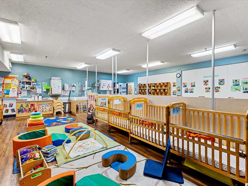 Classroom with multiple cribs, activity mats, and storage shelves