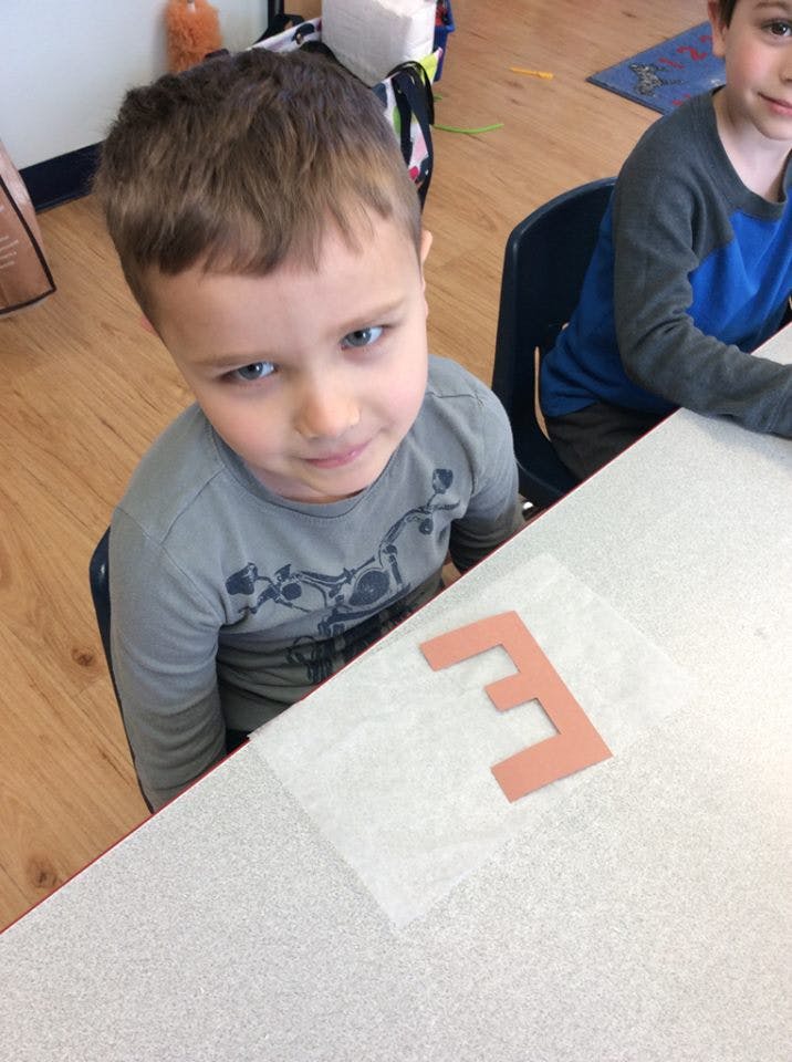 Child at a table with a letter E cutout