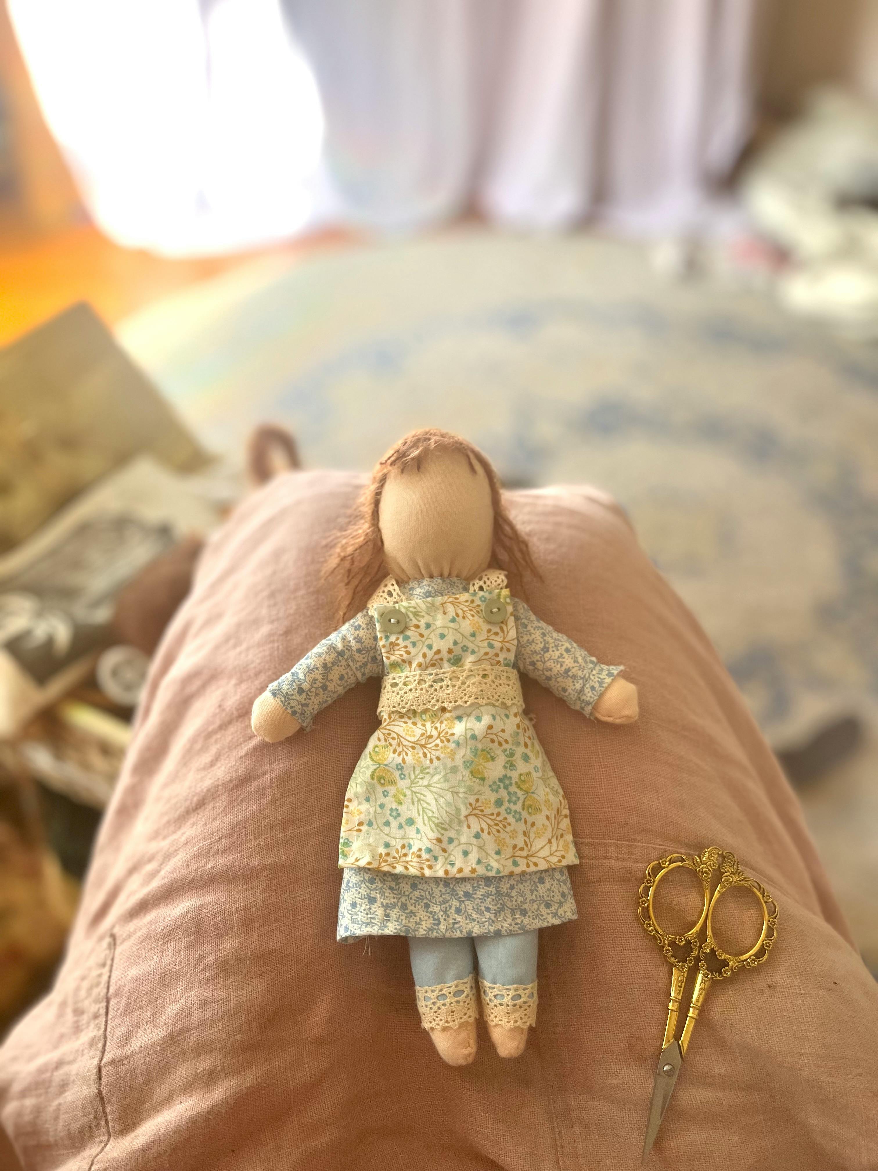 Handmade doll with a floral dress and a pair of scissors on a person's lap