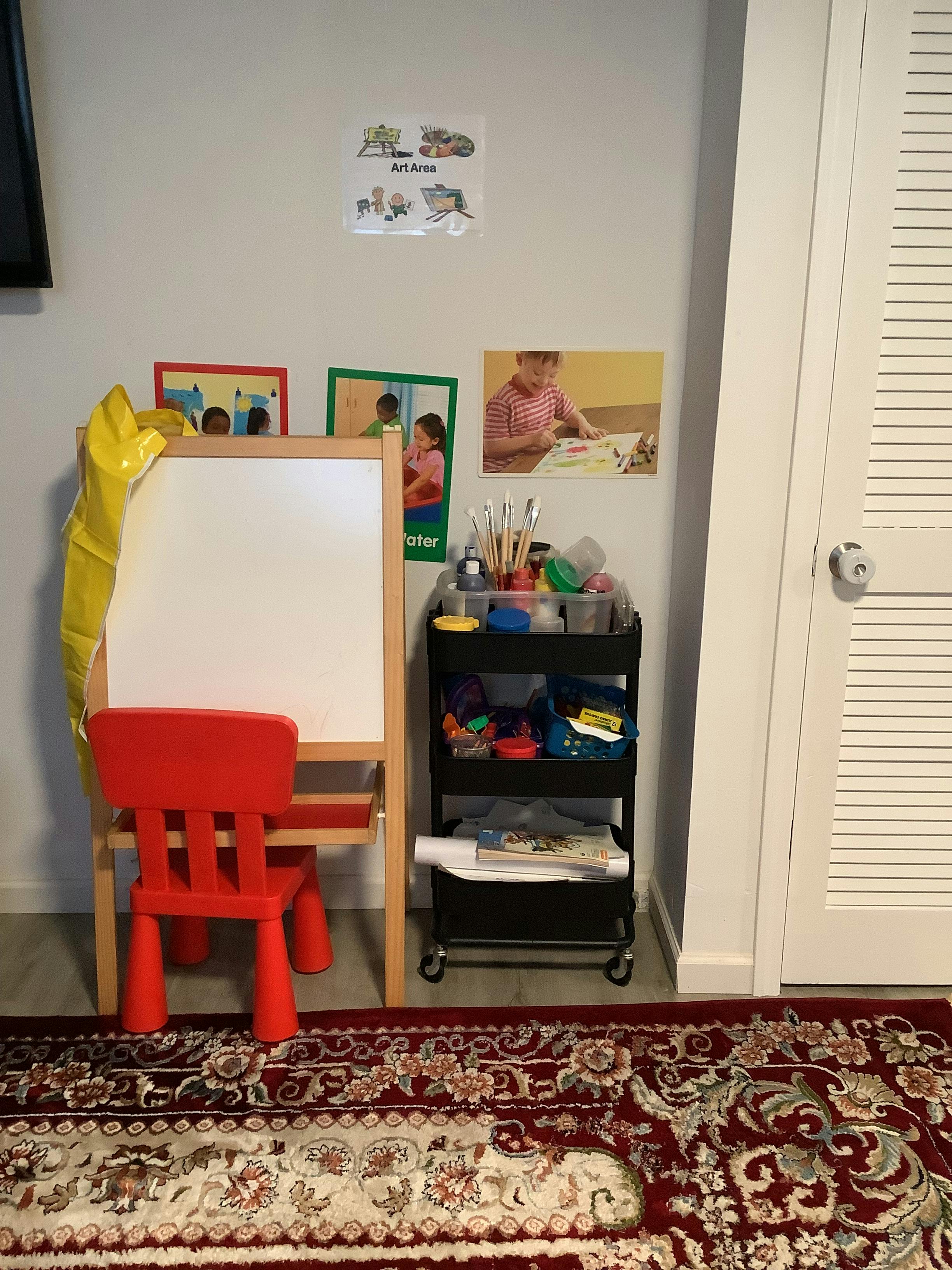 Easel with a red chair and a rolling cart with art supplies