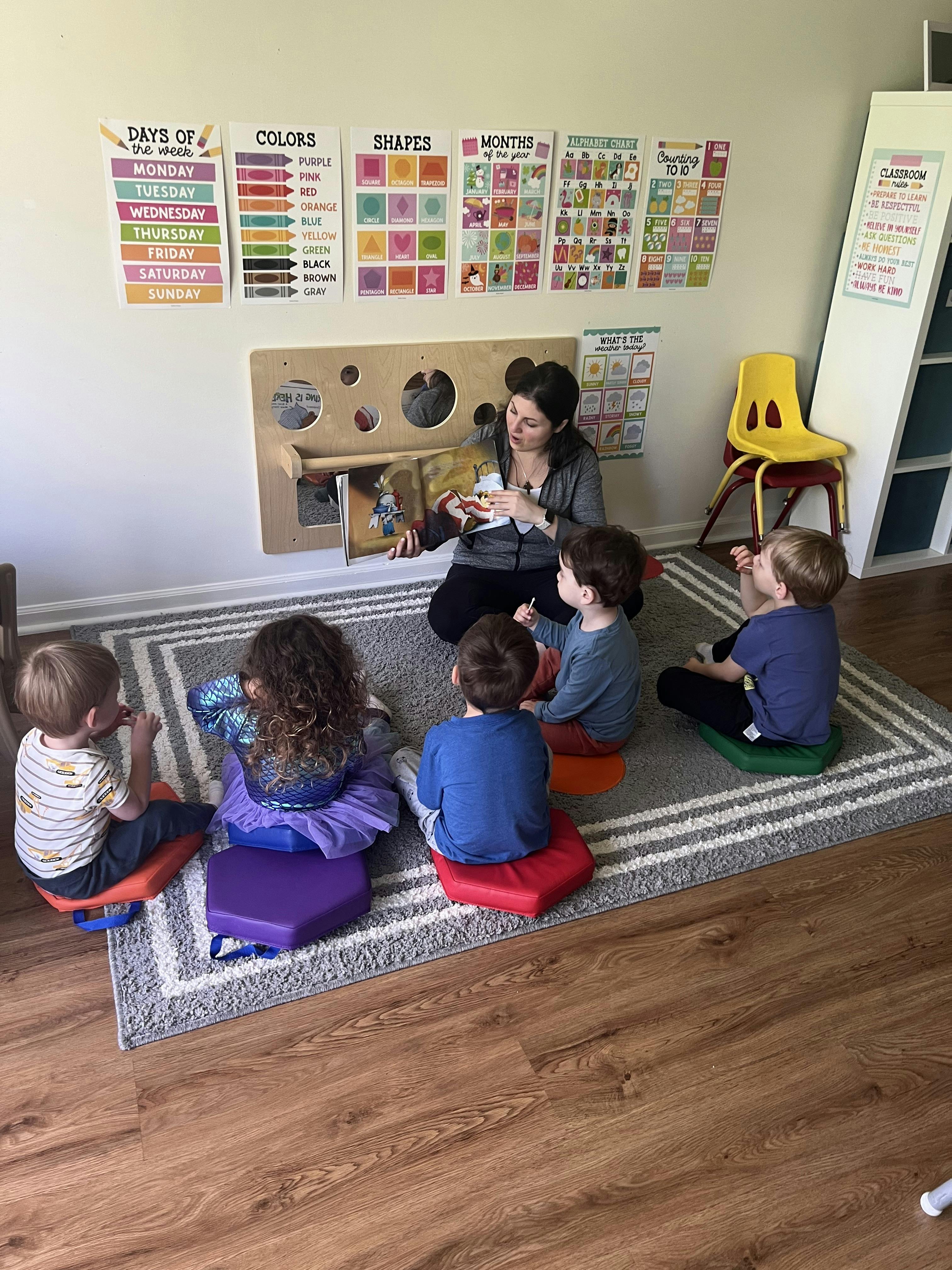 Person reading a book to several children sitting on cushions in a classroom