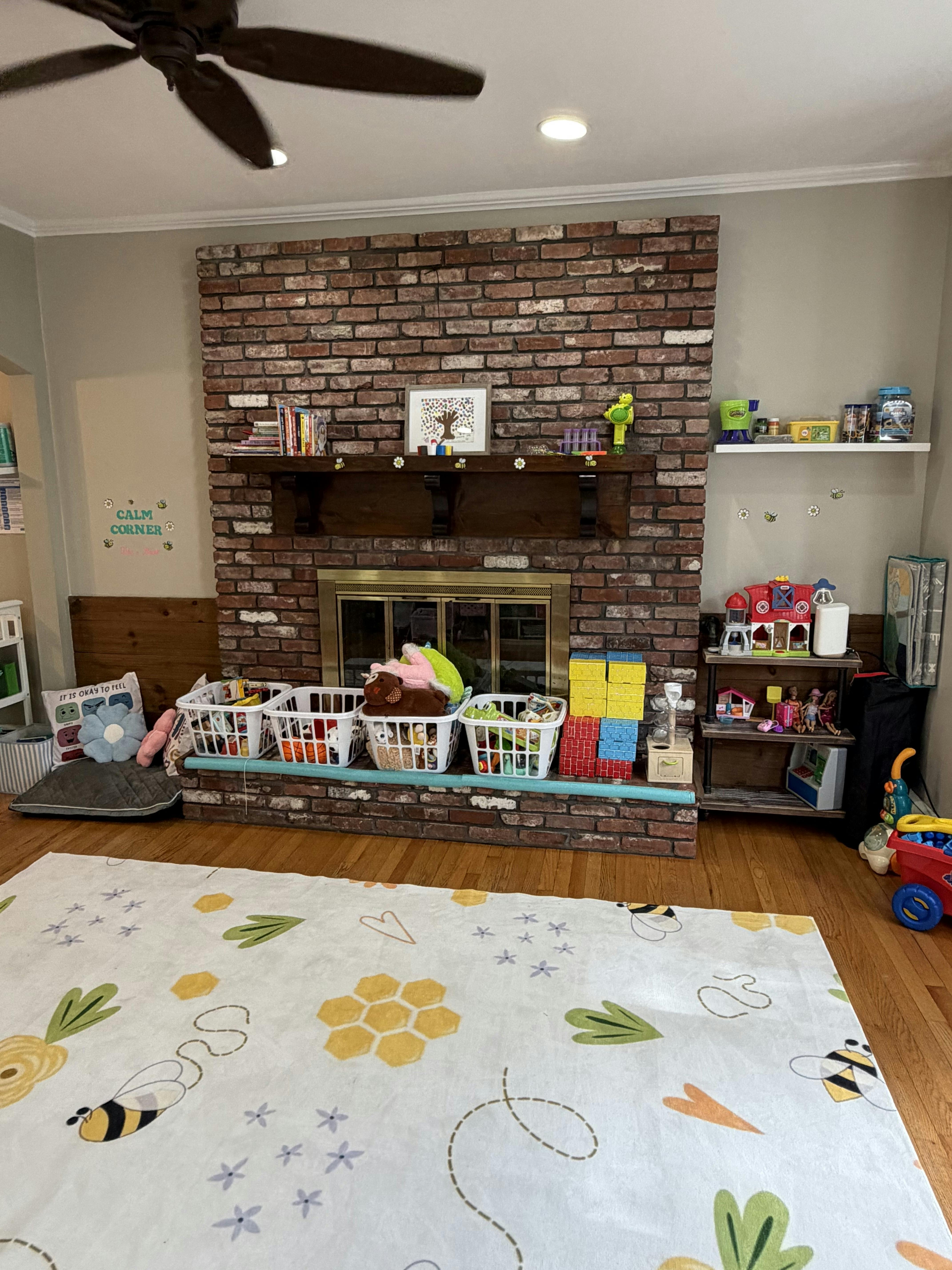Playroom with a brick fireplace and bins of toys sitting on a bee-themed rug