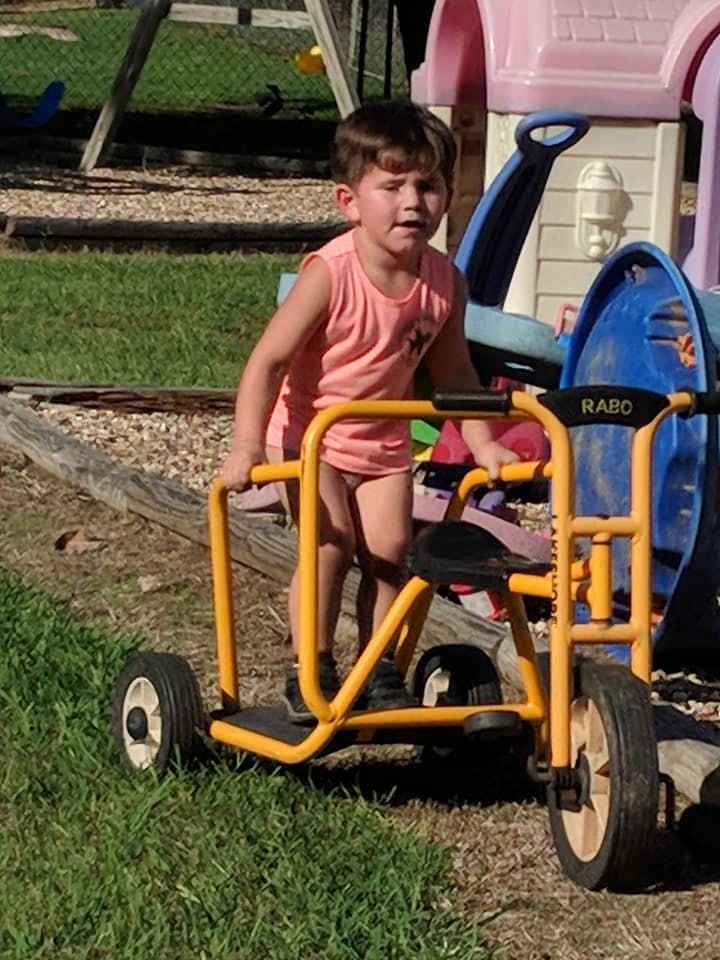 Child standing next to a yellow tricycle