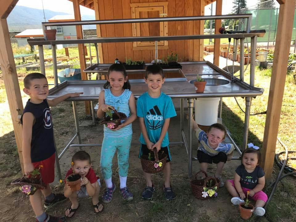 Six children holding potted plants and baskets with flowers