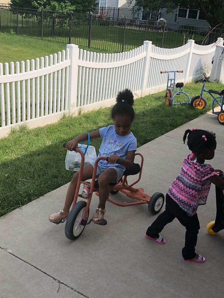 Child riding a tricycle on a sidewalk next to another child