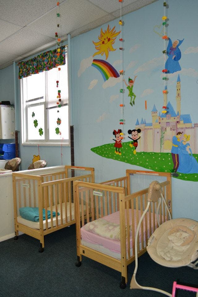 Two cribs in a room with a wall mural of cartoon characters