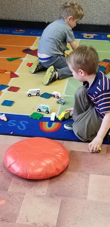Two children playing with toy cars on a colorful rug