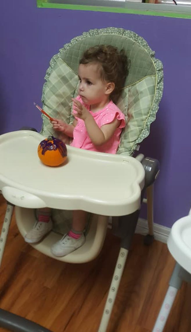 Child in a high chair holding a brush with a painted pumpkin on the tray