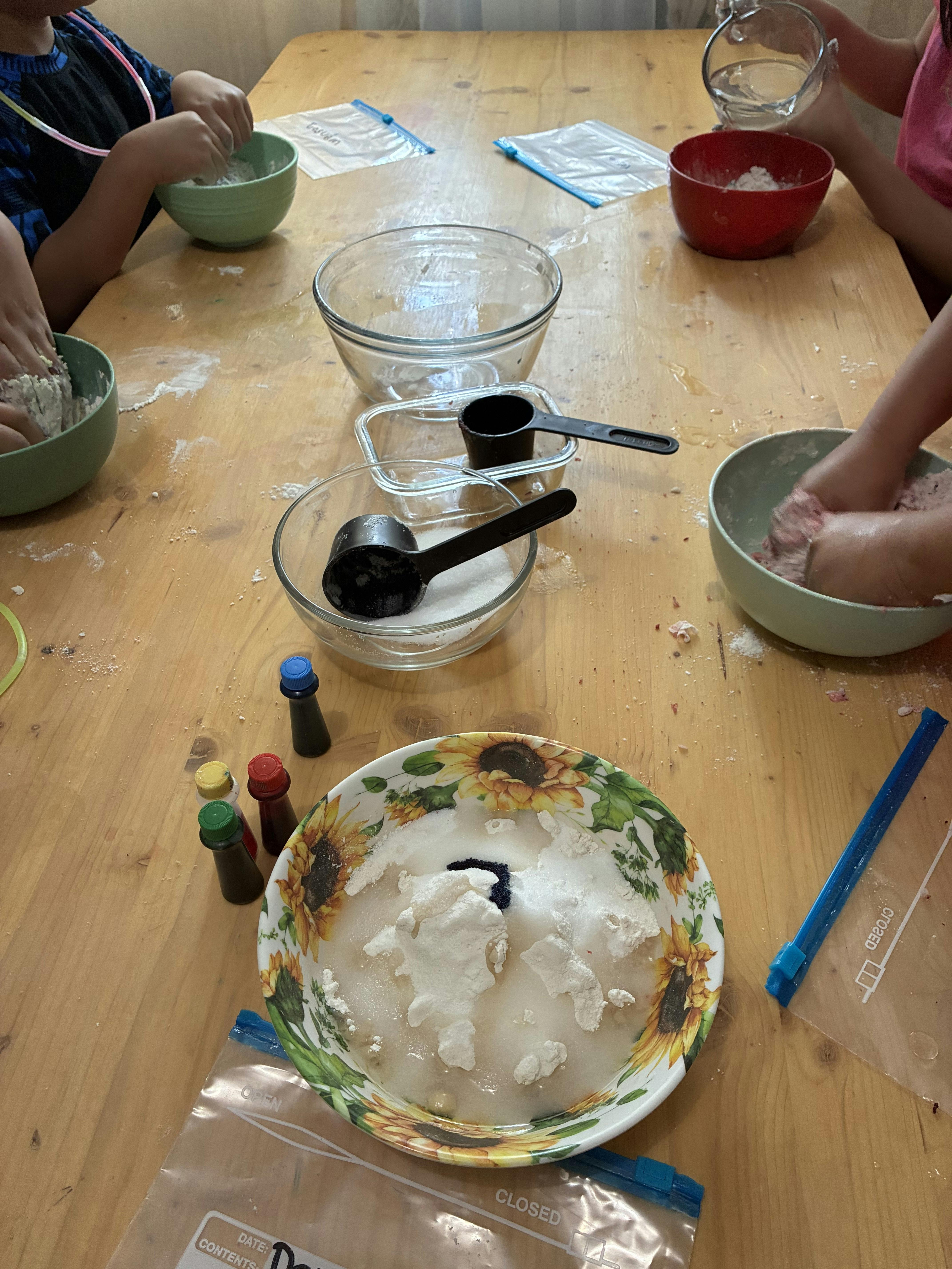 Multiple people making dough or slime at a wooden table