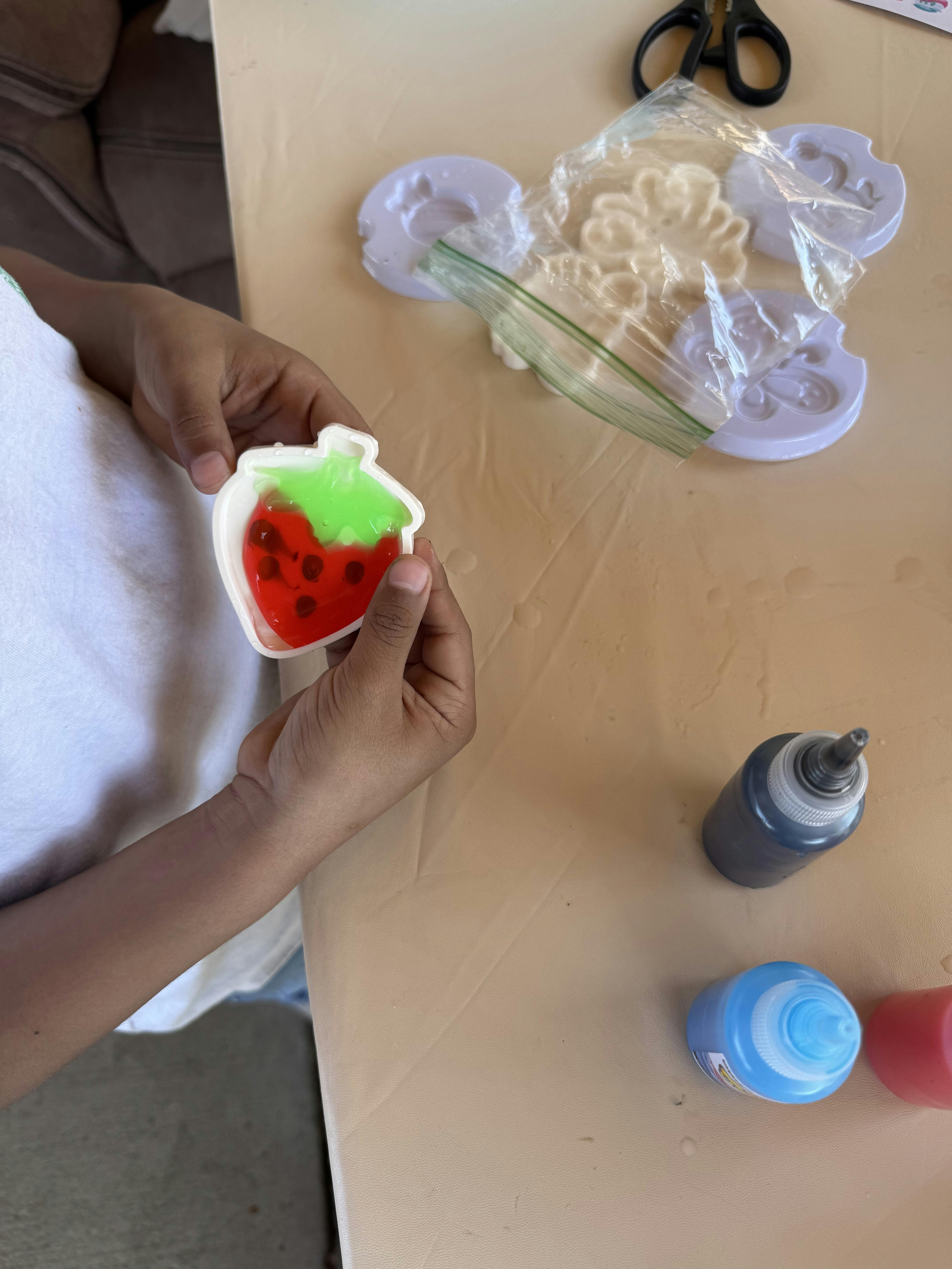 Child holding a strawberry-shaped mold with red and green liquid