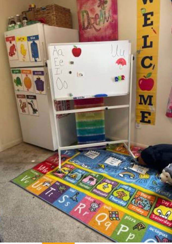 Whiteboard with letters and apple magnet next to a refrigerator with charts