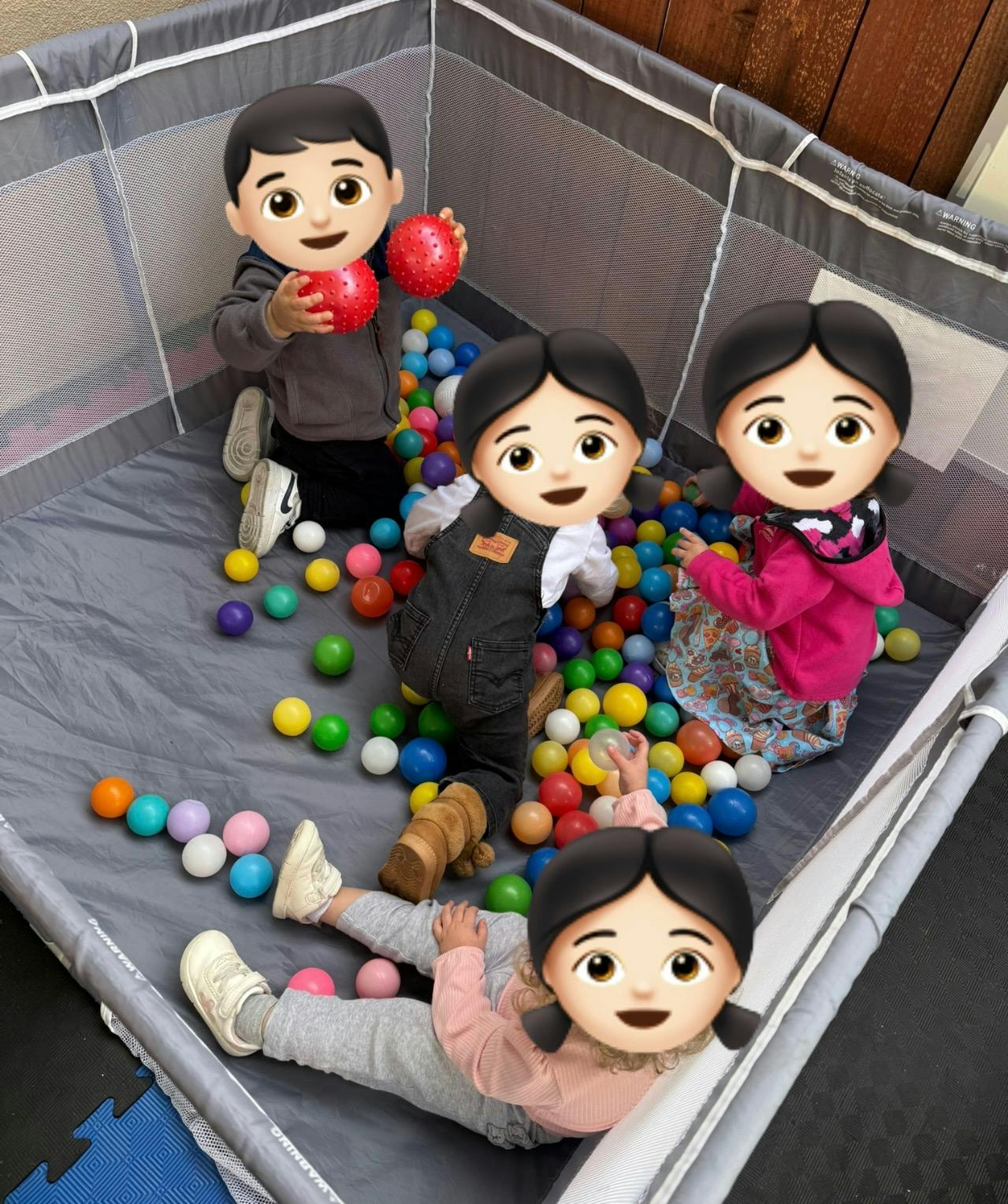 Four children in a playpen with colorful balls