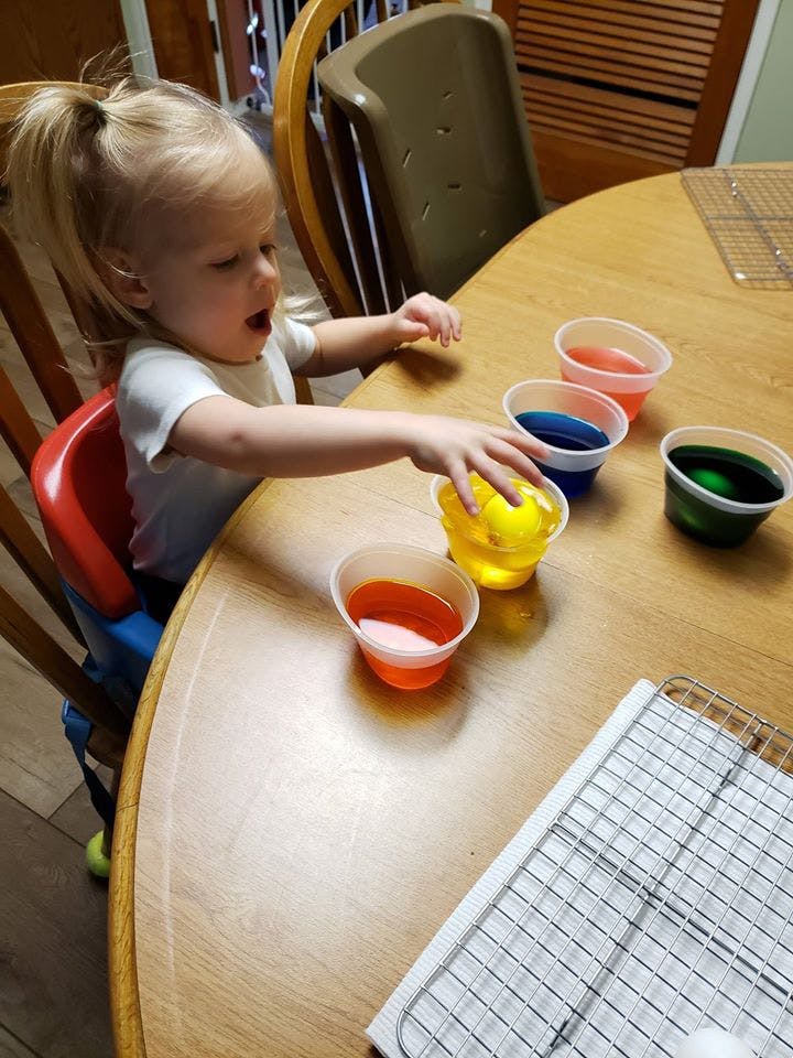 Child reaching for cups of colored liquid on a table