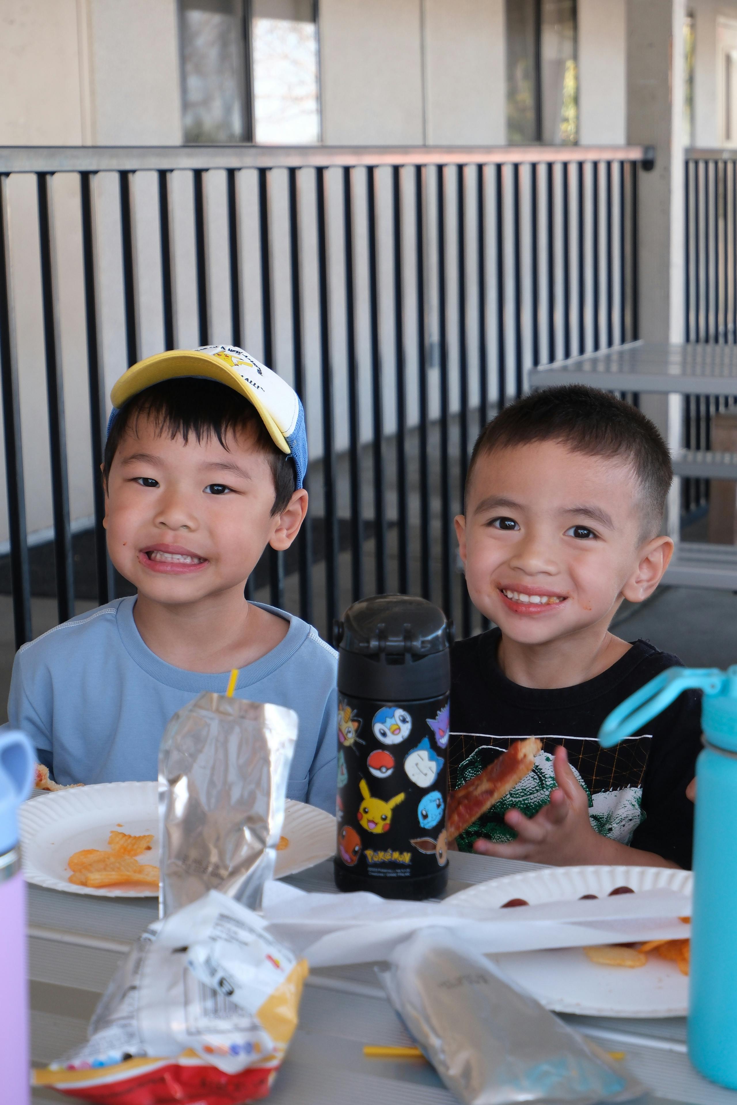 Two children eating snacks at a table outdoors