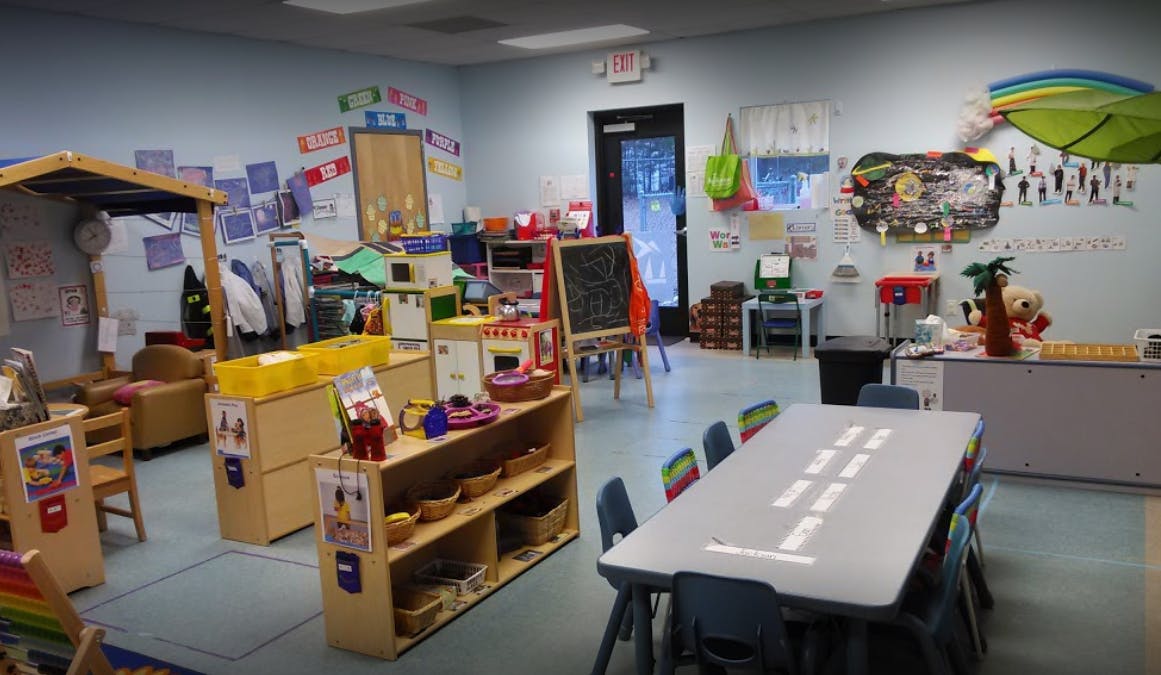 Classroom with small tables and chairs, shelves with toys, and a play kitchen