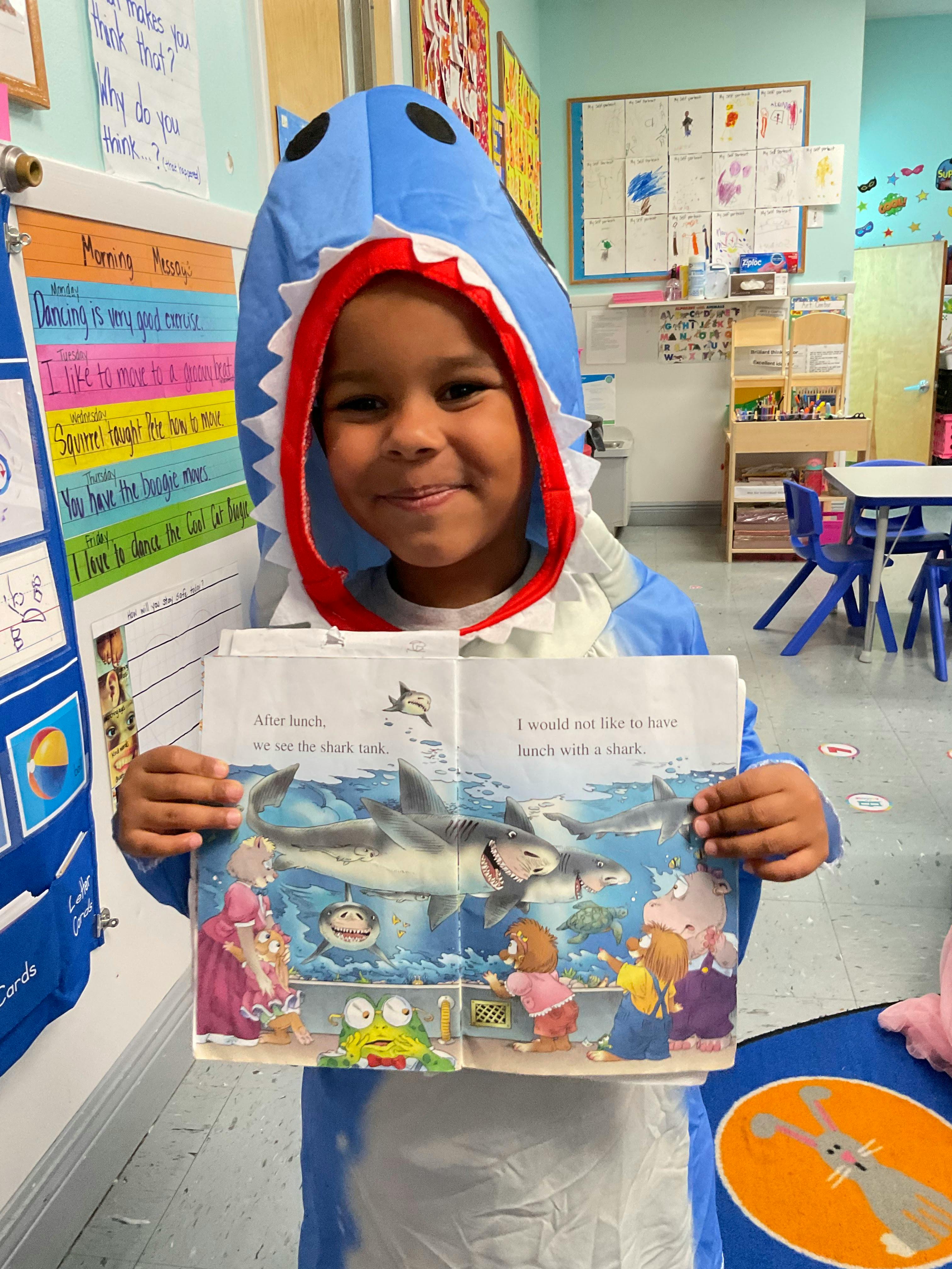 Child in shark costume holding an open book with an illustration of a shark
