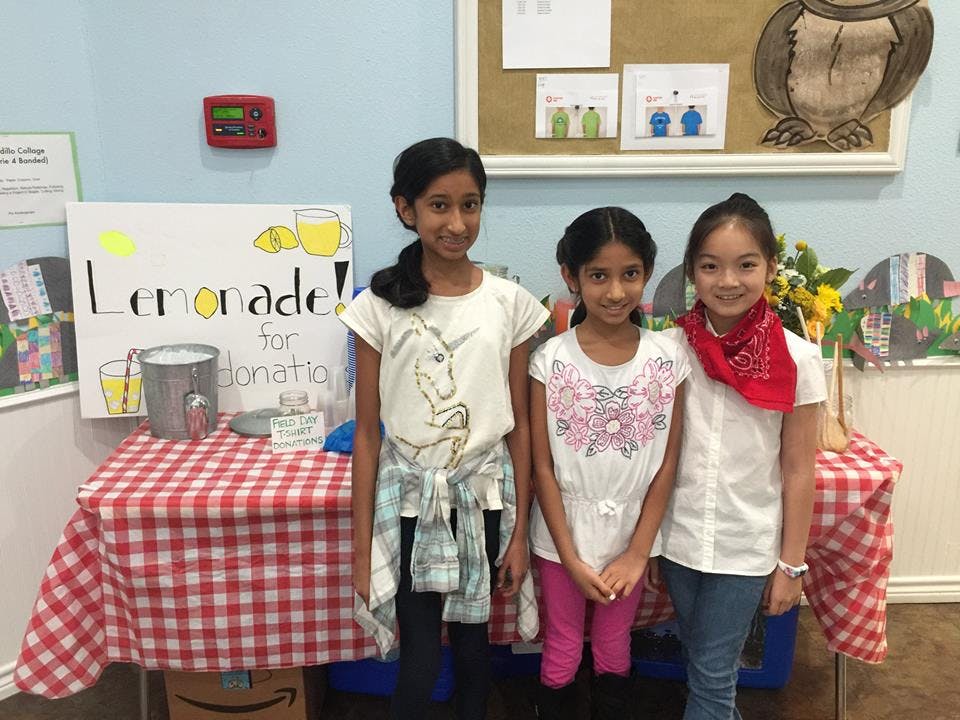 Three children standing in front of a lemonade stand