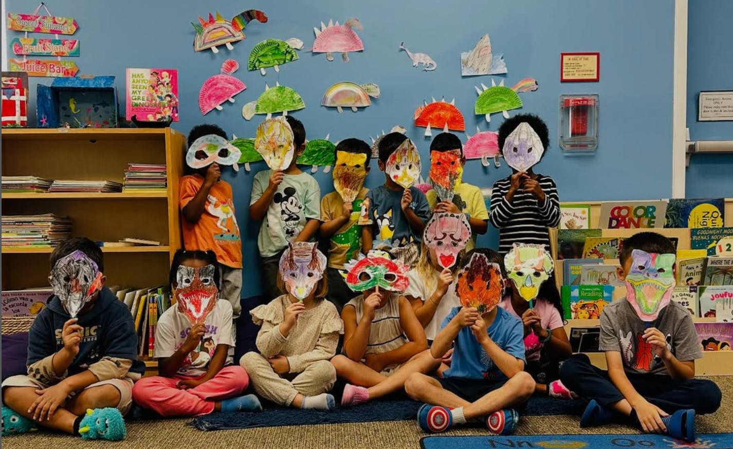 Group of children holding up handmade masks to their faces in a classroom