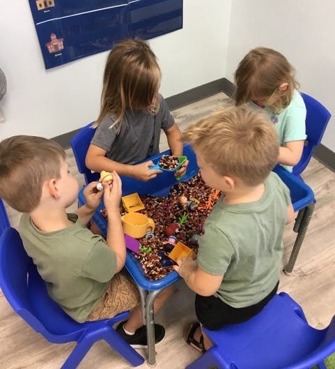 Four children playing at a table with sensory bins