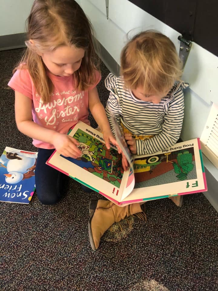 Two children sitting on a carpeted floor looking at a book together