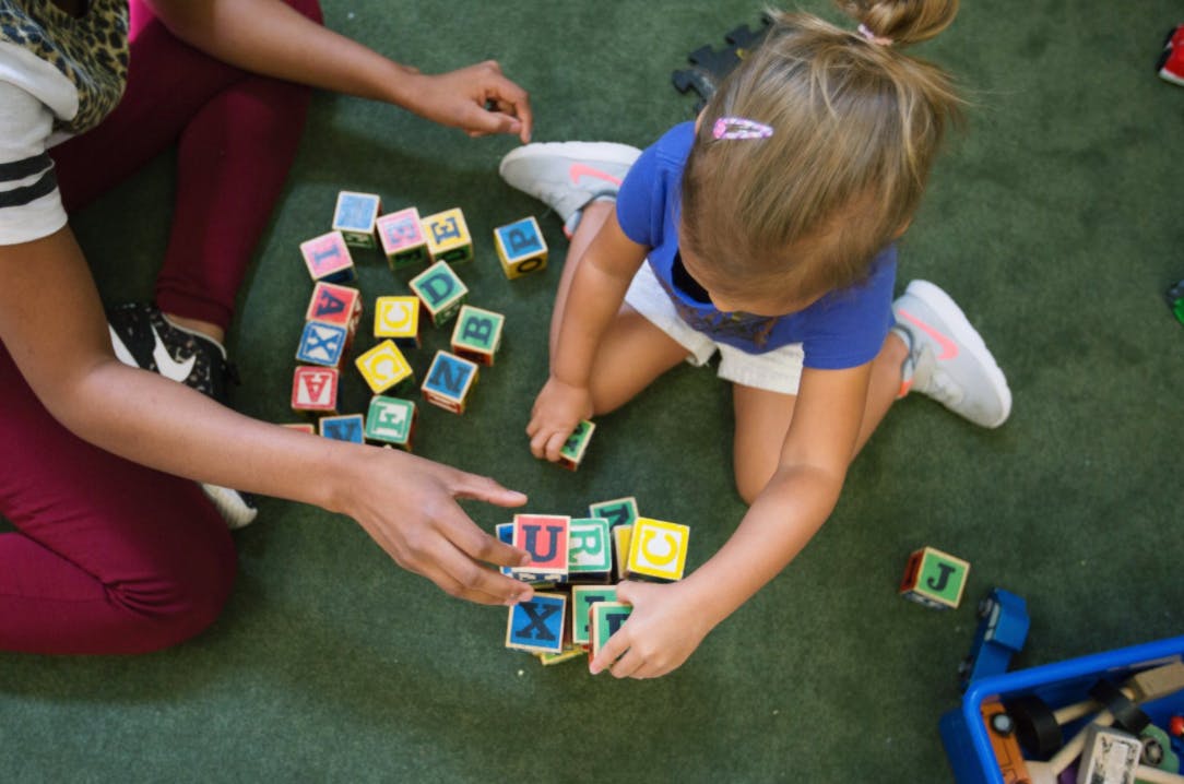 Person and child playing with alphabet blocks on the floor