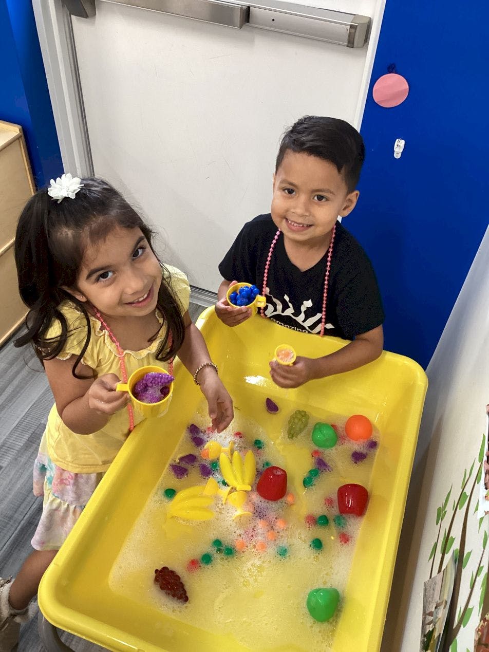 Two children playing with water and toys in a yellow bin