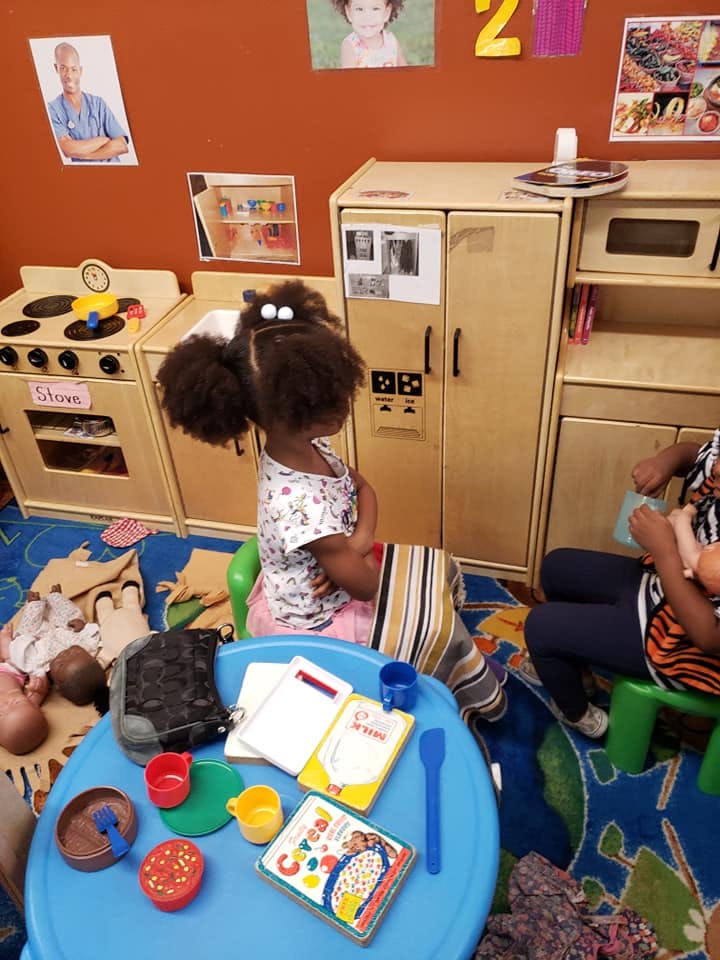 Child sitting at a blue play table with toy food and books