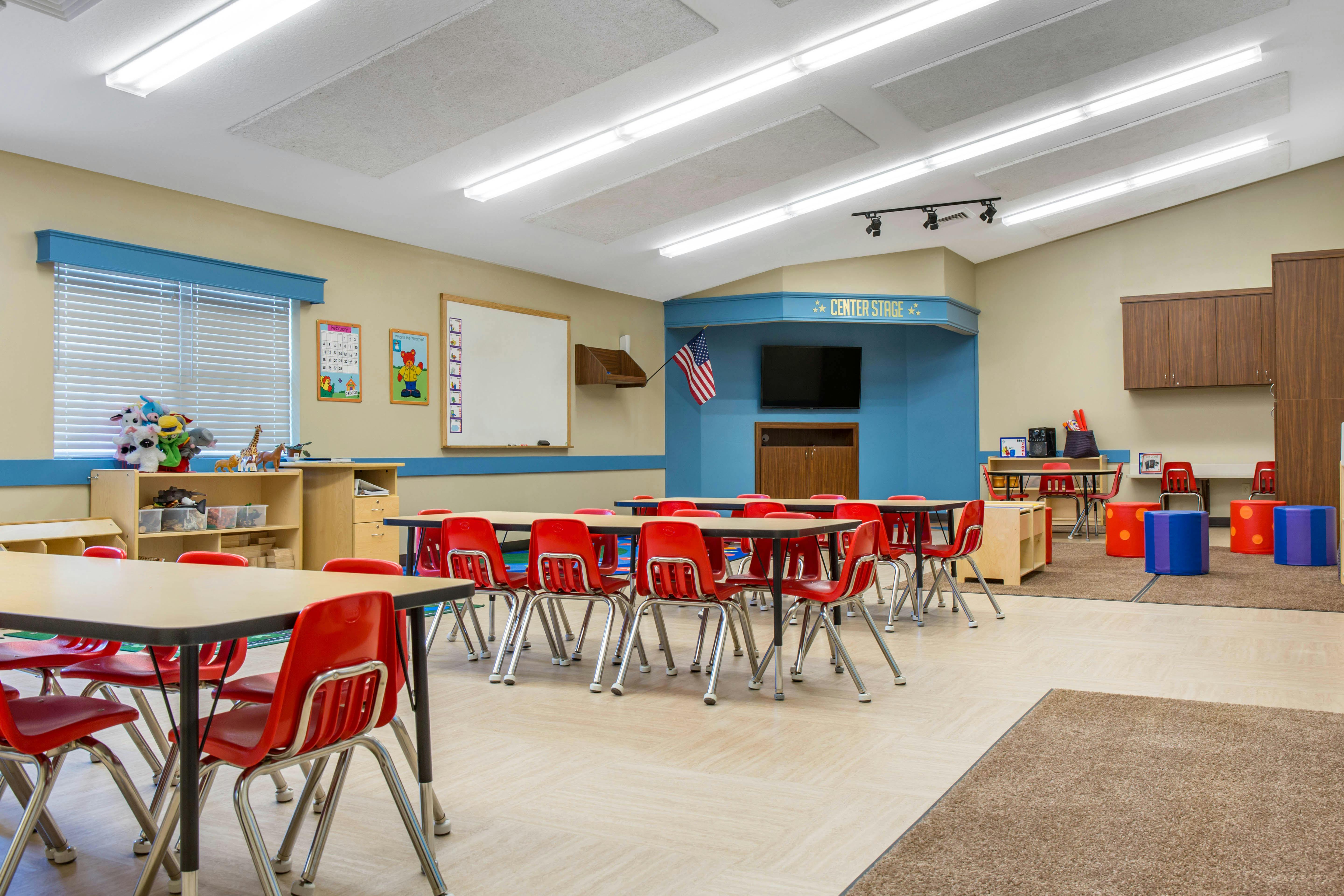 Classroom with small red chairs and tables, a TV, and an American flag