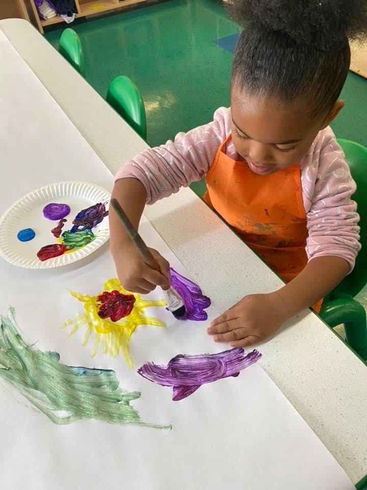 Child painting on paper with a brush in a classroom
