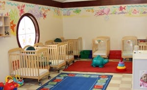 Nursery room with multiple cribs, a red rug, and a blue rug