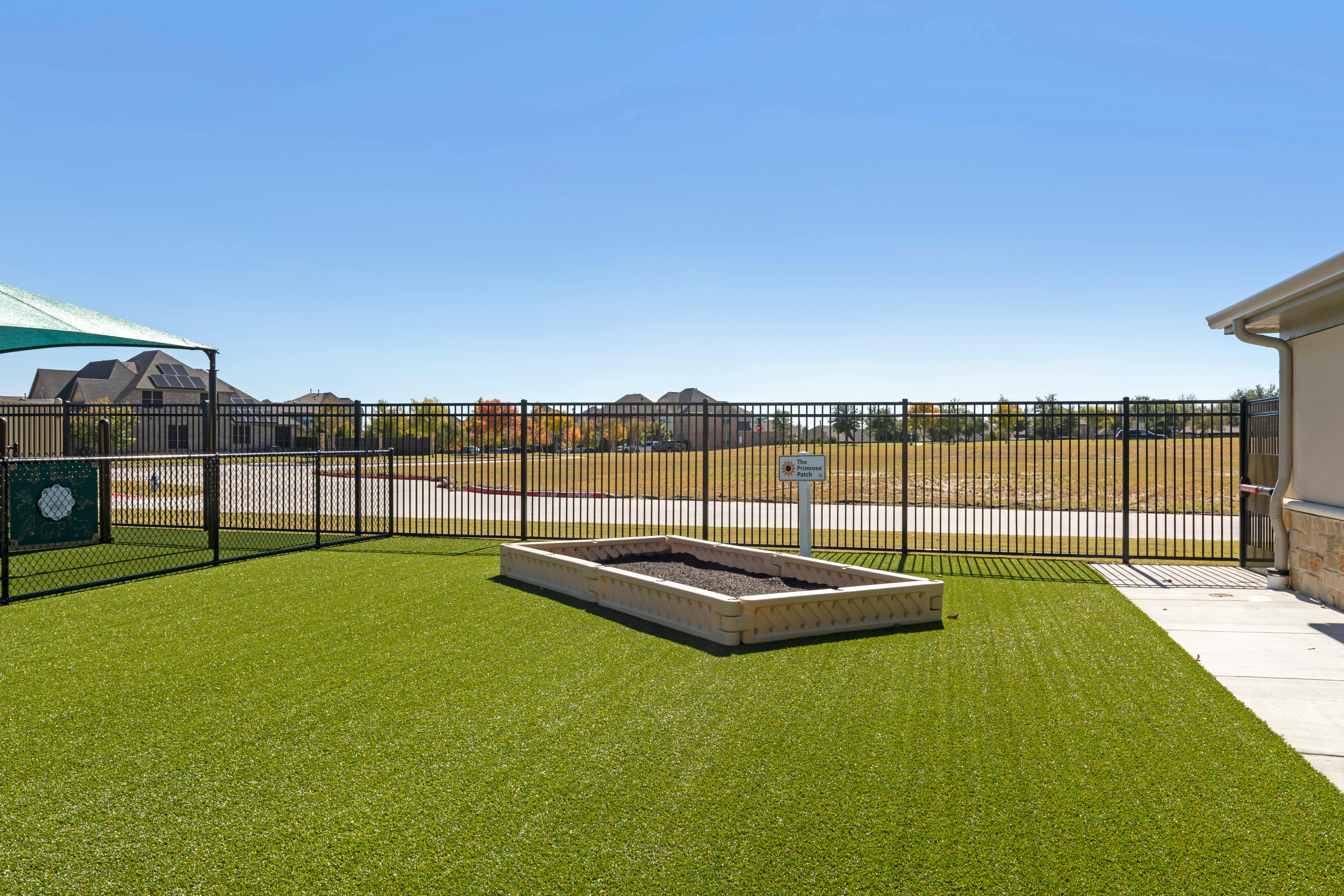An outdoor area with artificial turf, a black fence, and a raised garden bed