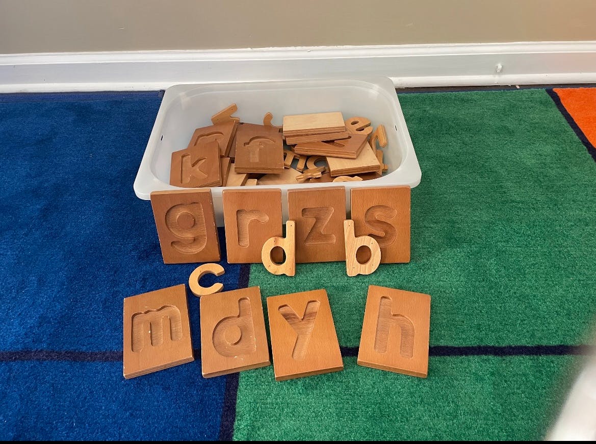 Wooden letter cutouts and blocks in a container on a rug