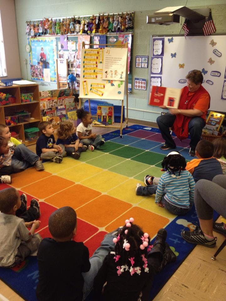 Adult reading a book to children sitting on a rainbow rug in a classroom