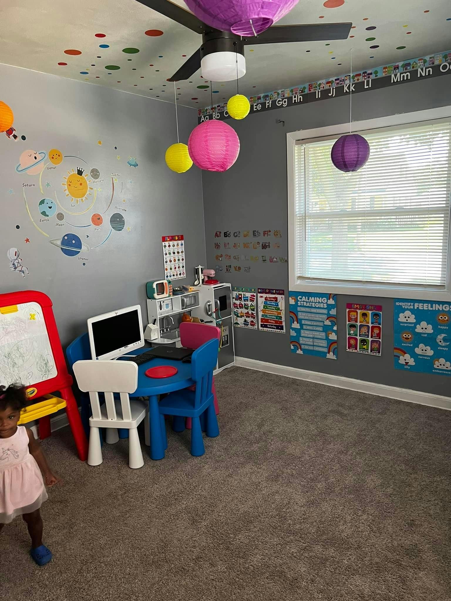 Child standing in a room with a small table and chairs, and wall decorations