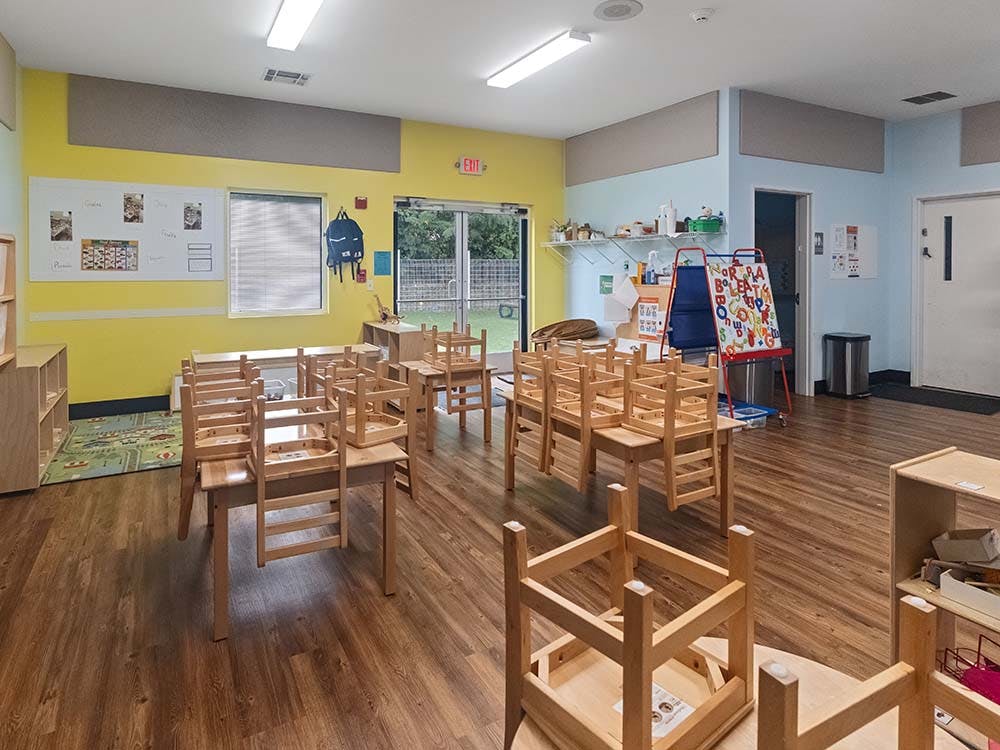 Classroom with small wooden tables and chairs, whiteboard, and easel