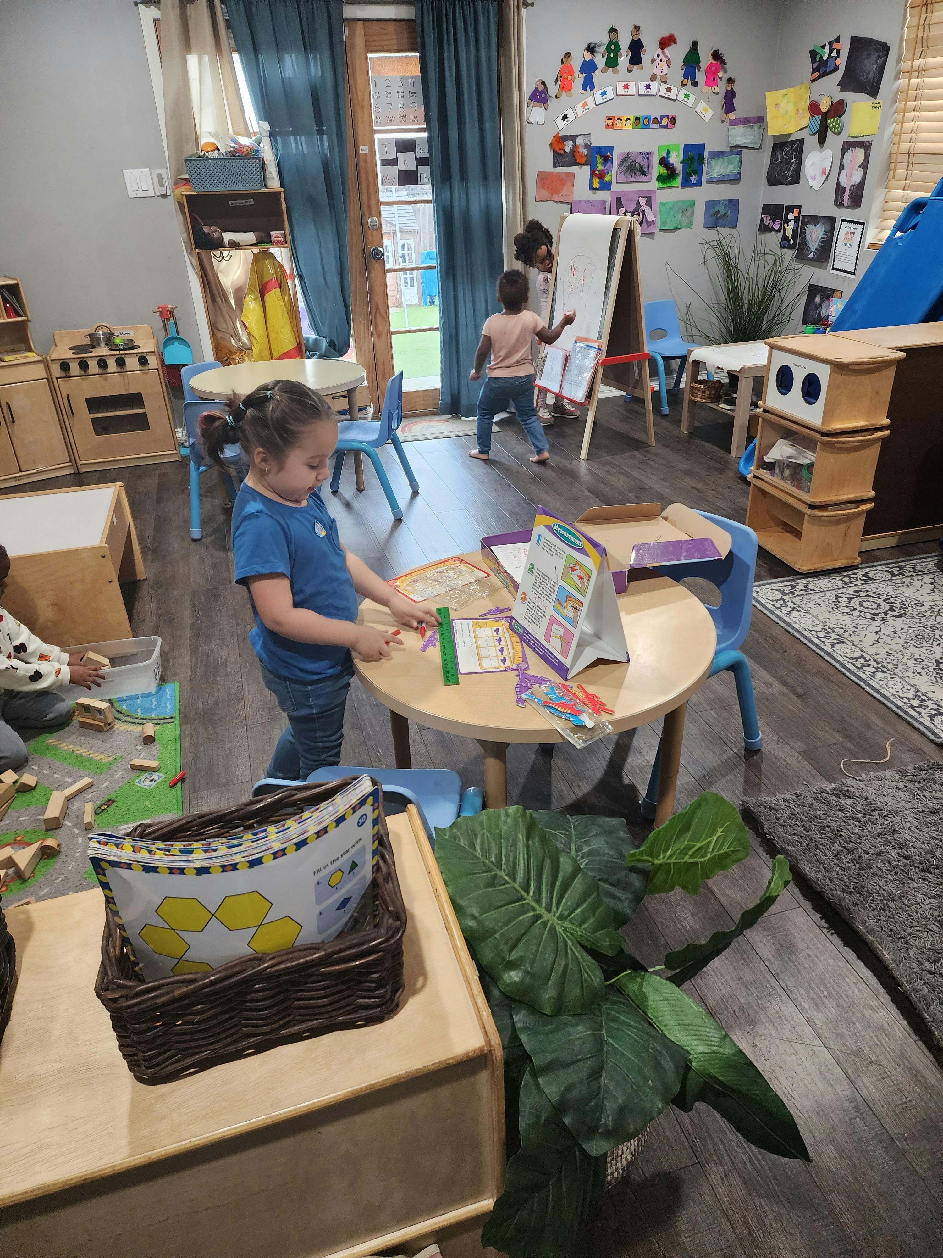 Child at a table with another child at an easel in a classroom