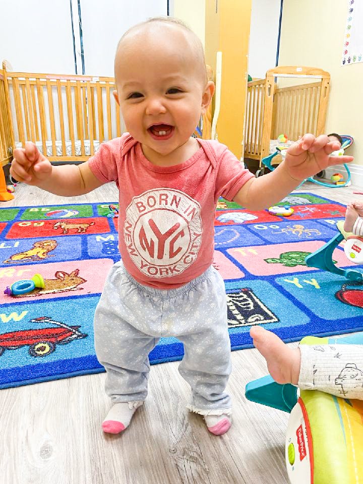 Child standing on a colorful rug in a room with cribs