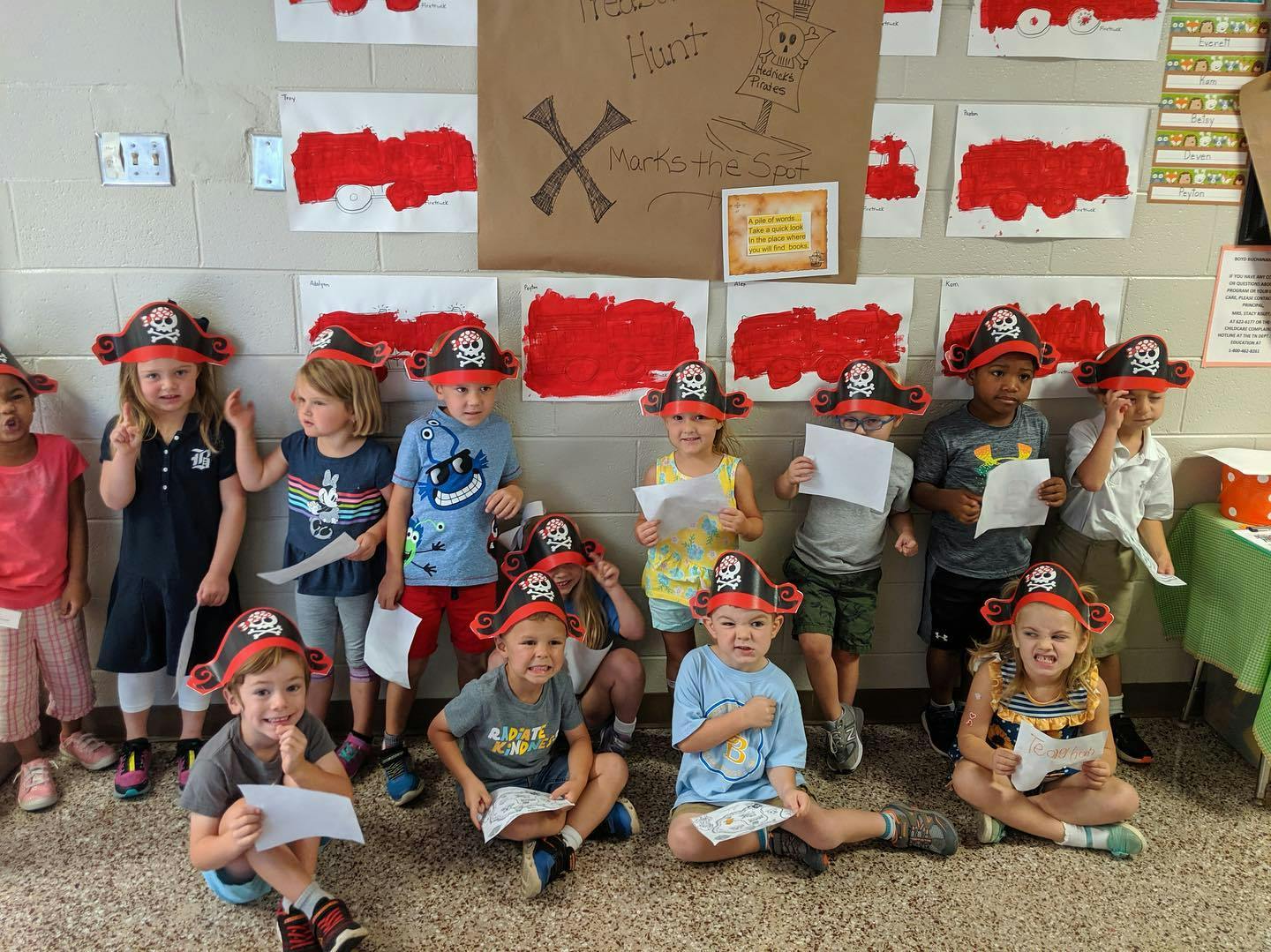 Children in pirate hats holding papers in a classroom
