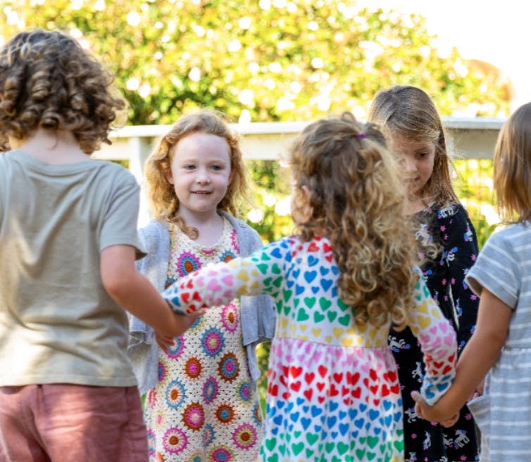 Five children holding hands in a circle outdoors in a circle