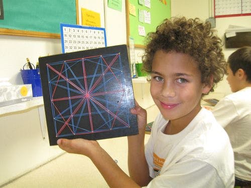 Child holding up a string art board with red and blue threads