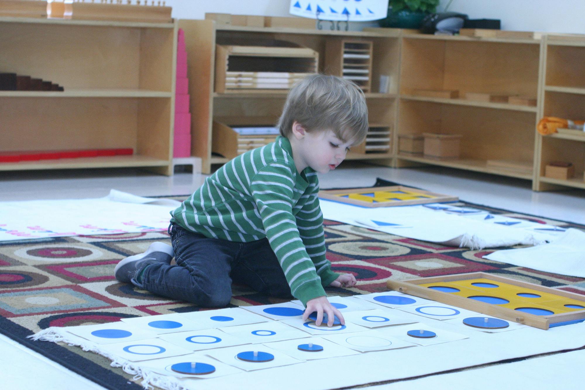 Child kneeling on a rug, placing a blue circle onto a white board