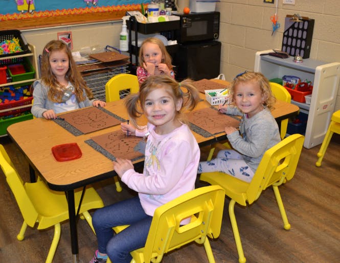 Four children sitting at a table in a classroom