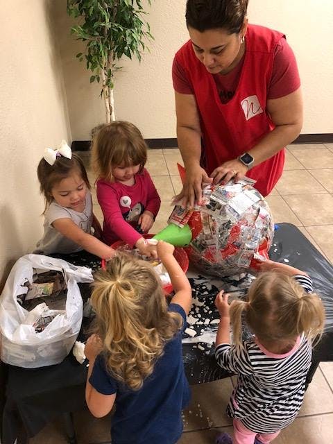 Person and three children decorating a large object with paper and glue