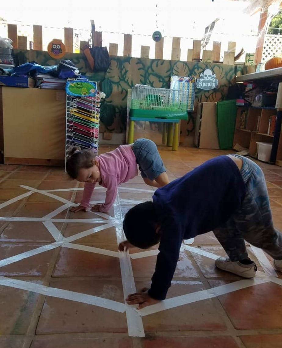 Two children crawling on a floor with white tape lines