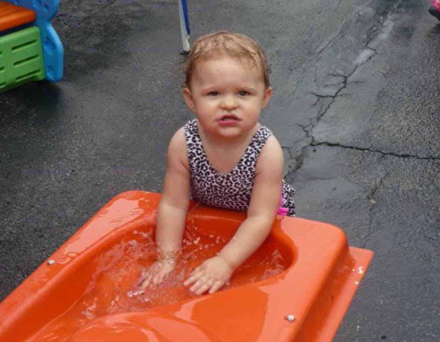 Child in a swimsuit playing in water in an orange container