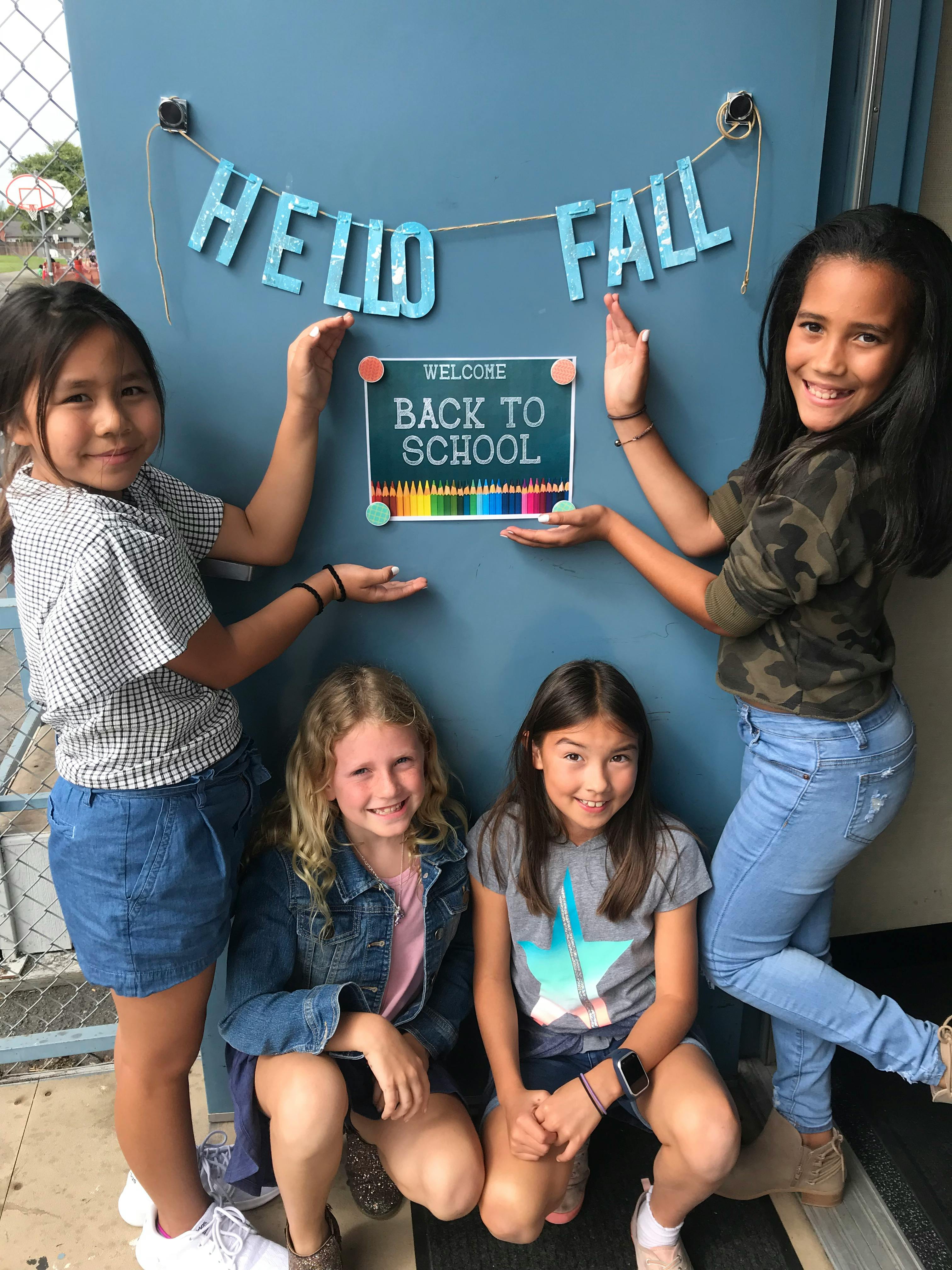 Four children posing with a "Welcome Back to School" sign and "Hello Fall" sign