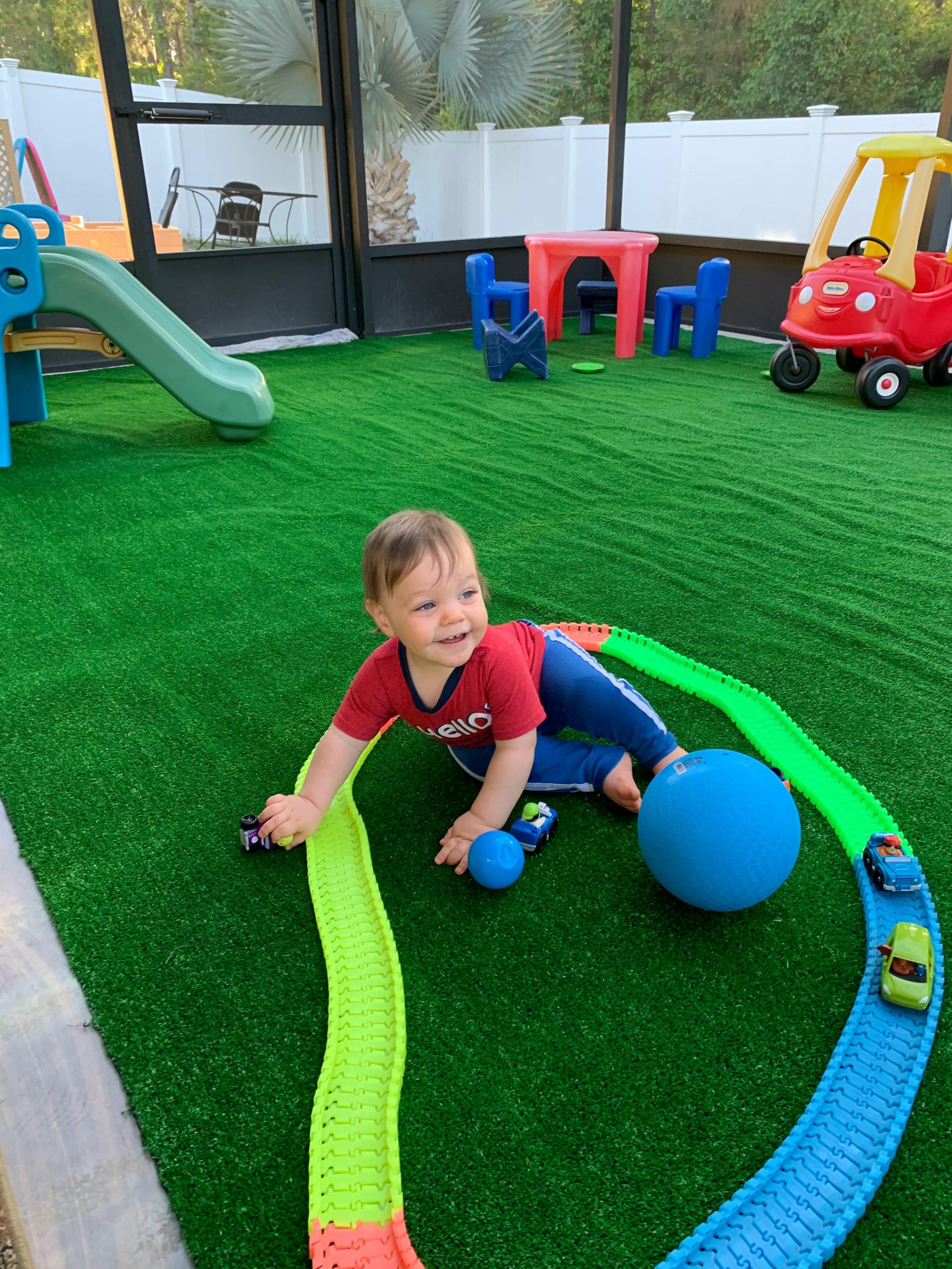 Child playing with toy cars on a track on artificial grass
