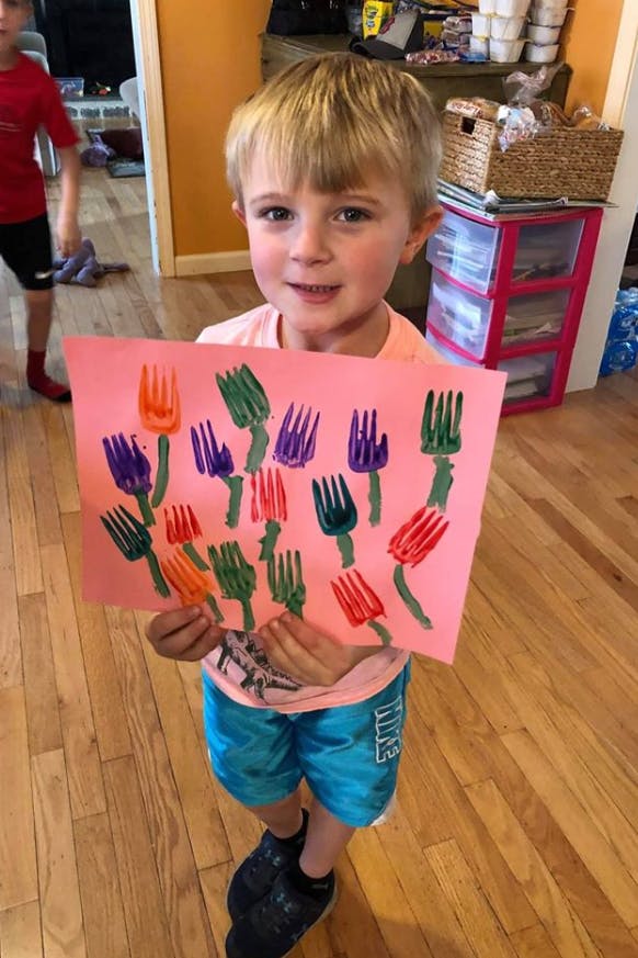 Child holding up a piece of paper with colorful fork prints