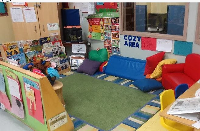 Classroom reading nook with a green rug, blue and red seating, and books