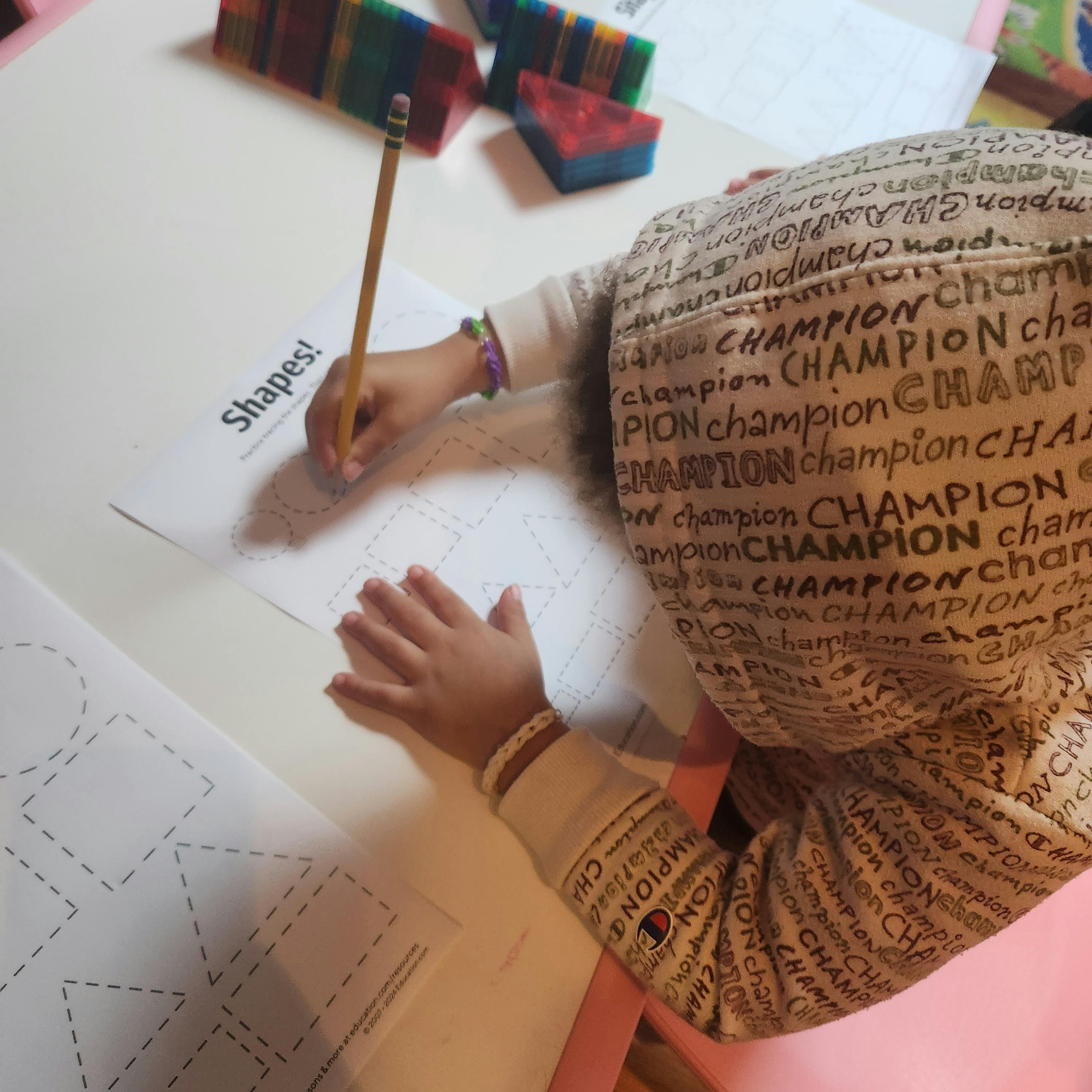 Child tracing shapes on a worksheet with a pencil